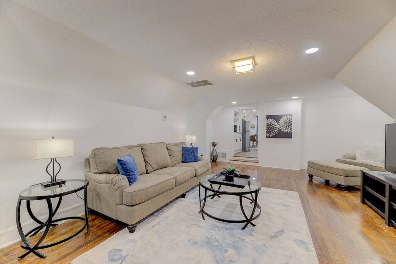 A spacious living area with a sofa, coffee table, and TV stand. A staircase leads to an upper floor.