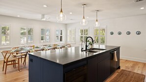A modern kitchen with a central island, wooden dining table, and chairs. - Zen-N-Sea offers poolside relaxation and near the beach entrance, sleeps 8 (St Simons Island)
