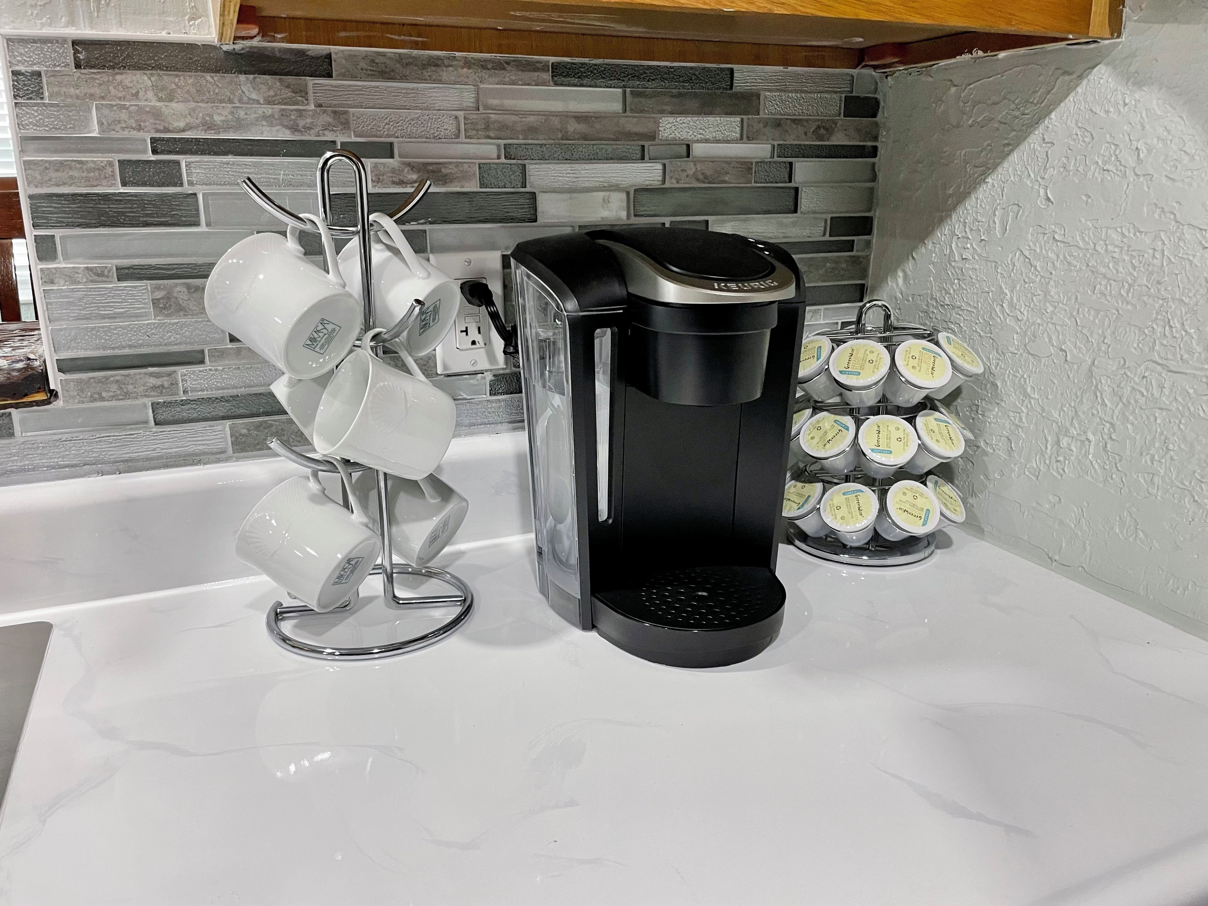 A kitchen with a coffee maker, a mug rack, and a container of coffee pods.
