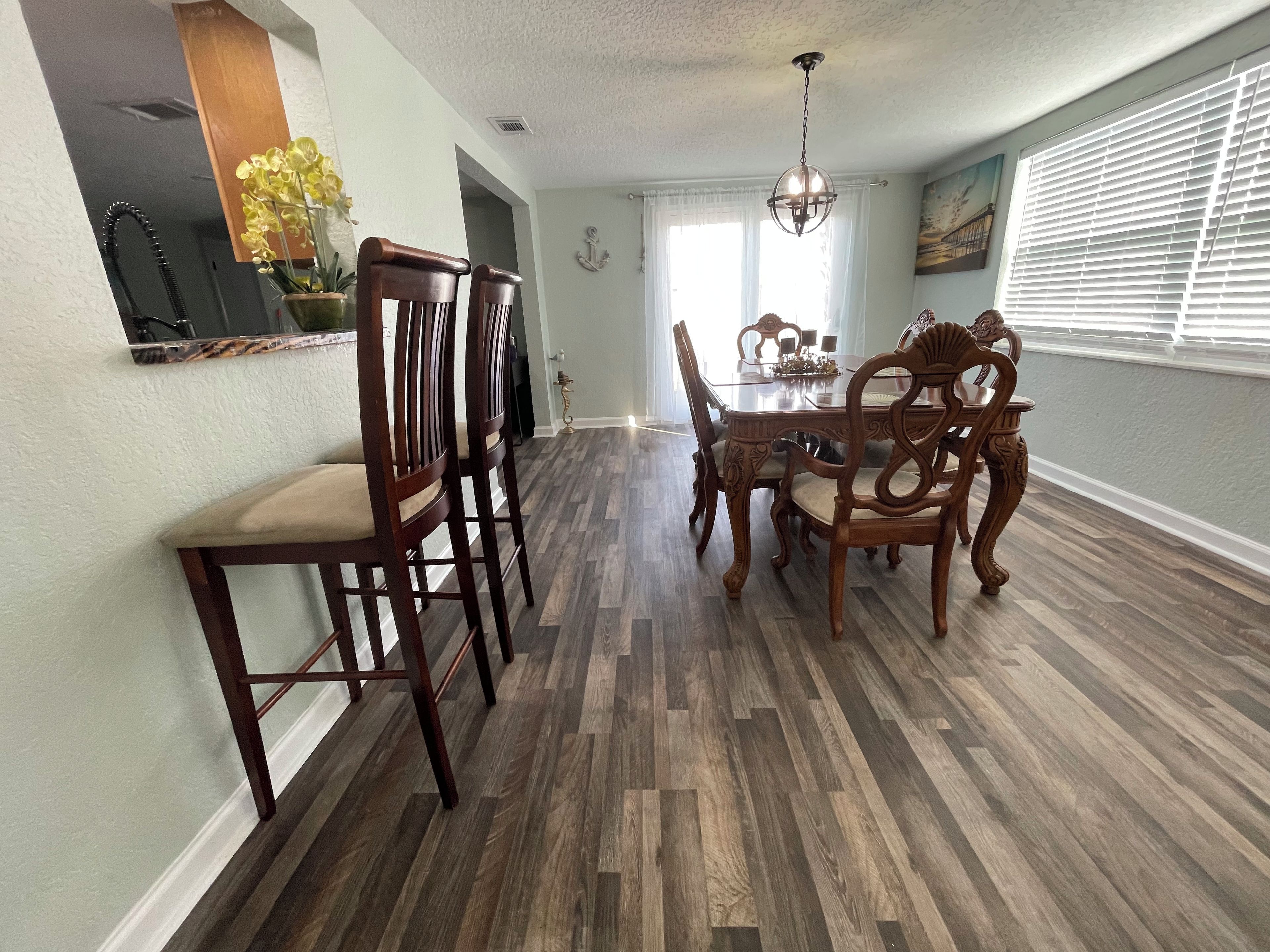 A dining area with a wooden table and chairs, a chandelier, and a window with blinds.