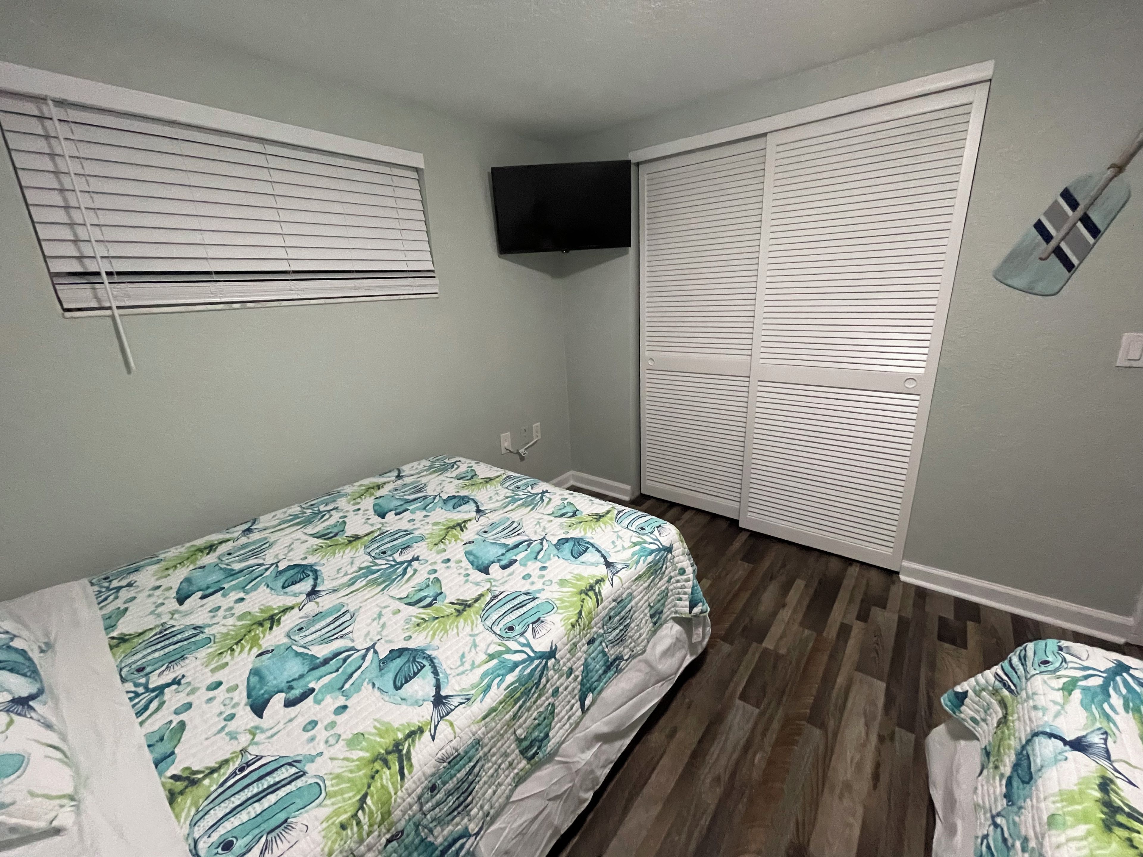 A bedroom with a bed, a TV mounted on the wall, and a closet with sliding doors.