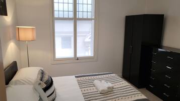 A bedroom with a bed, a nightstand, a lamp, a window, and a wardrobe.