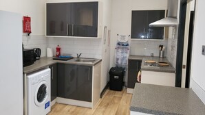 Et kompakt køkken med vaskemaskine, elkedel og lille bordplade.