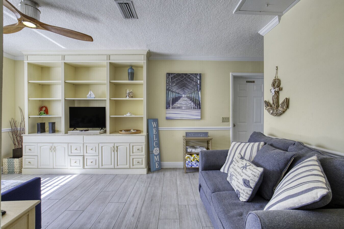 A living room with a built-in entertainment unit, a gray sofa with striped cushions, and a wooden floor.