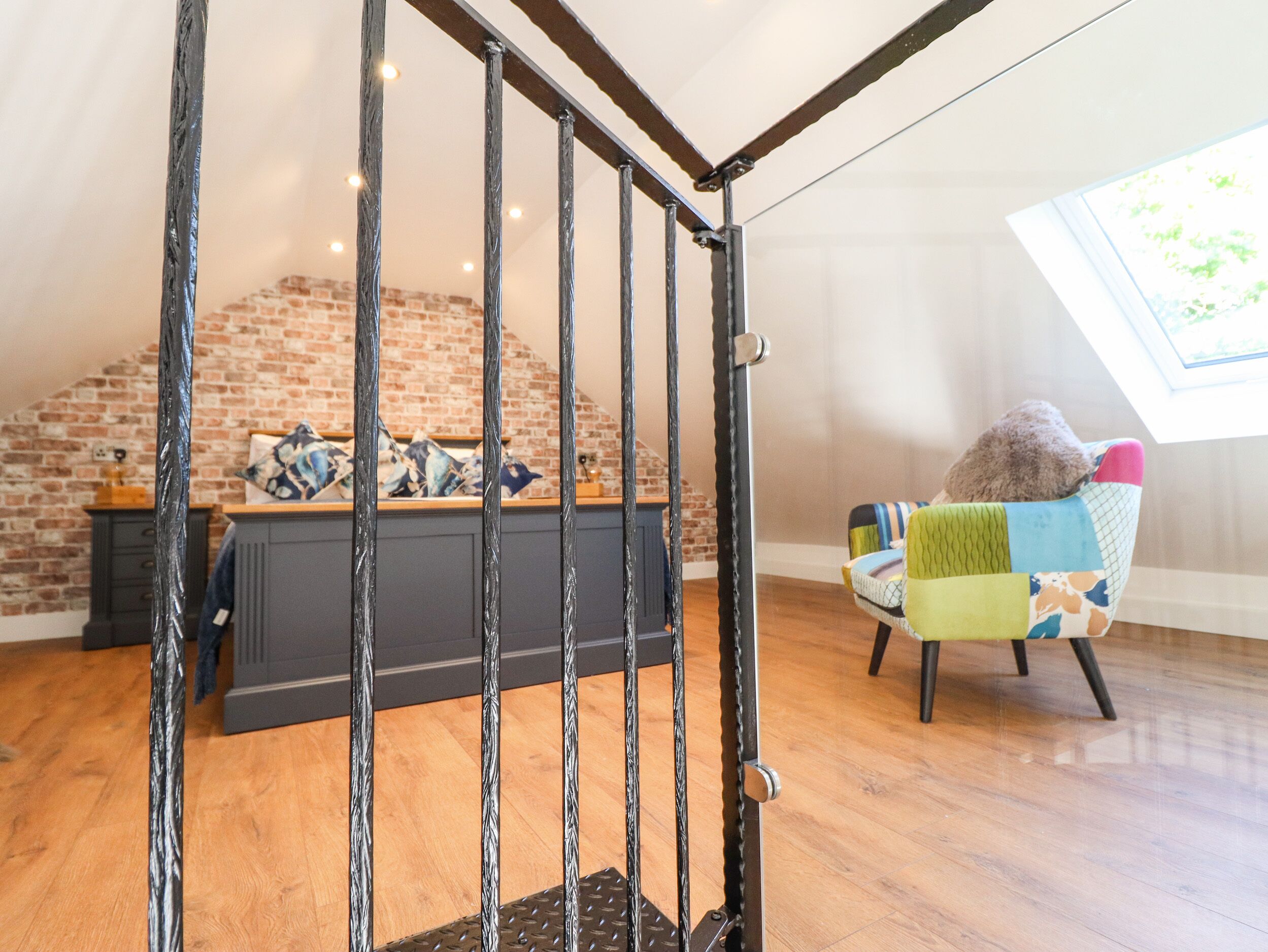 A staircase with a metal railing leading to a room with a brick wall and a window.