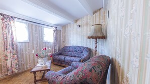 A room with floral wallpaper, a sofa, a chair, a table with a vase, and a lamp. - House l'oustaou les 2 oliviers (Moustiers-Sainte-Marie)