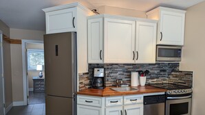 Cocina moderna con armarios blancos, un refrigerador de acero inoxidable, un microondas, una cafetera y un lavavajillas.