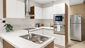 A modern kitchen with white cabinetry, stainless steel appliances, and a central island with a sink. - Mabaat - Al Malqa - 384 (Riyadh)