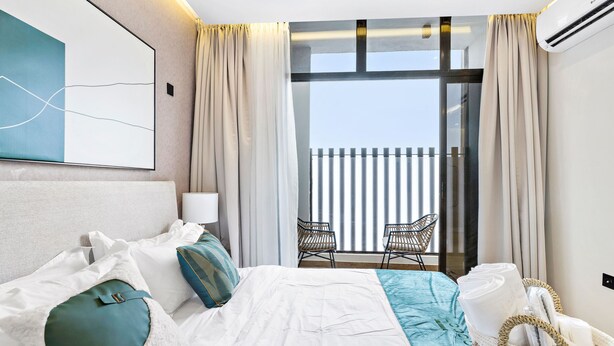 A hotel room with a large bed, a view of the balcony, and a wicker basket with towels. - Mabaat - Al Malqa - 384 (Riyadh)