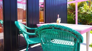 A patio with wicker chairs and a table, a bottle of wine, and a view of a garden through a window. - Zen Garden Cottage - Sleeps 2 - Patio & Parking (Poole)