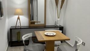 Un espace repas moderne avec une table en bois, deux chaises grises, un lampadaire, un miroir et des plantes décoratives.