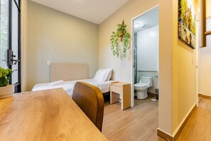 Ein Hotelzimmer mit Bett, Schreibtisch, Stuhl, einer kleinen Topfpflanze und Blick ins Badezimmer.