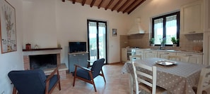 A kitchen with a TV, a dining table, chairs, a fireplace, and a window with curtains.