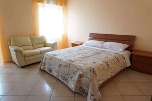 A bedroom with a bed, a nightstand, a chair, and a window with curtains.