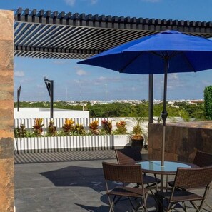 Eine Terrasse im Freien mit Tisch, Stühlen und einem blauen Sonnenschirm, mit Blick auf die Stadtlandschaft.