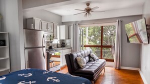 Un dormitorio compacto con cama, sofá, kitchenette y un ventanal grande.