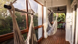 Una terraza de madera con dos hamacas, una silla y vistas a la vegetación a través de amplios ventanales.
