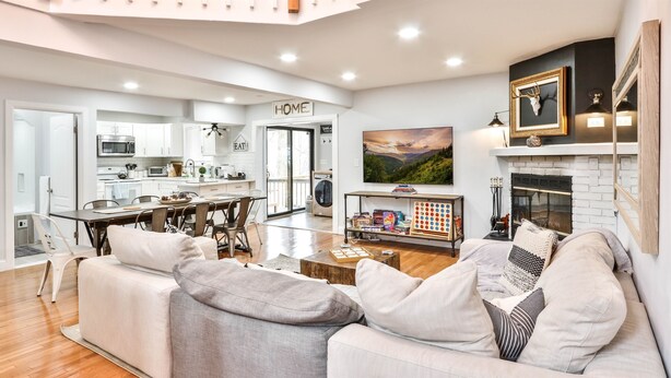 Ein modernes Wohnzimmer mit Sofa, Couchtisch und Kamin. Im Hintergrund ist eine K üche mit einem 'HOME'-Schild zu sehen.