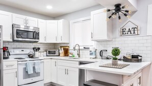 Eine moderne Küche mit weißen Schränken, einer Edelstahl-Mikrowelle, einem Backofen, einem Spülbecken und einer Arbeitsplatte mit verschiedenen Geräten und Küchenutensilien.