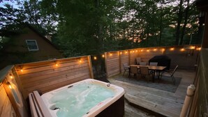Ein Whirlpool auf einer Holzterrasse mit Tisch und Stühlen, umgeben von Lichterketten.