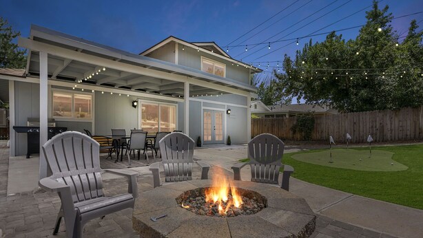 Un patio con un hogar para la leña, mobiliario exterior e una zona cubierta con guirnaldas de luces.