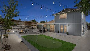 Una casa de dos pisos con un patio, mobiliario exterior y un césped cuidado.
