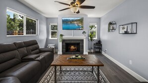 Una sala de estar moderna con chimenea, ventilador de techo y un televisor grande montado sobre ella.