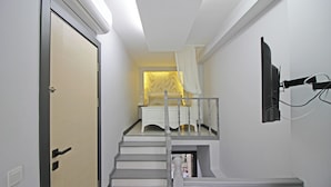 A staircase with a white railing, a door with a black handle, and a wall-mounted television. - Seher Hanim Konagi (Bozcaada)