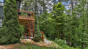 A wooden deck with a staircase leading to a second level, surrounded by dense forest. - Private Renovated home 1.5 Miles to downtown Highlands!  (Highlands)