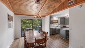 A spacious dining area with a wooden table and chairs, a kitchen with grey cabinets, and a large window overlooking greenery. - Private Renovated home 1.5 Miles to downtown Highlands!  (Highlands)