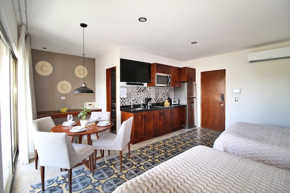 A hotel room with a dining area, kitchenette, and two beds.