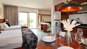 Une chambre d’hôtel avec deux lits, une table à manger dressée pour quatre personnes, un coin cuisine et un balcon avec vue.