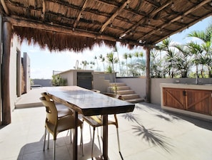 A covered outdoor patio with a table and chairs, a staircase, and a view of palm trees.