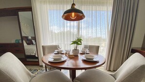 Un coin repas avec une table ronde en bois, mise pour deux personnes, deux chaises rembourrées, une plante en pot et un luminaire suspendu.
