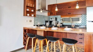 Une cuisine moderne avec des meubles en bois, un îlot central doté de tabourets, un four à micro-ondes et une machine à café.