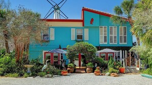 A turquoise building with a windmill, red shutters, and outdoor seating.