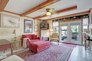 A cozy living room with a red sofa, a wooden ceiling, and a large window with a view of greenery. - Windmill Gardens Inn "Gallery" by Galveston Bay is a cozy tropical hideaway! (San Leon)