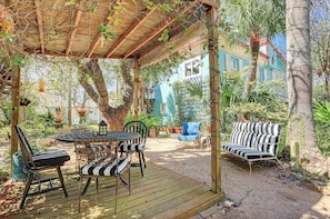An outdoor patio with a wooden table and chairs, a blue sofa, and a striped bench. - Windmill Gardens Inn "Gallery" by Galveston Bay is a cozy tropical hideaway! (San Leon)