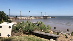 A coastal view with a pier extending into calm waters, surrounded by greenery and a wooden deck.