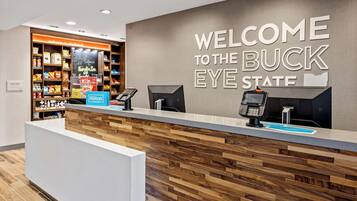 Un mostrador de recepción de hotel con un cartel que dice 'Welcome to the Buck Eye State', una mini nevera y un cartel de Hilton Honors.