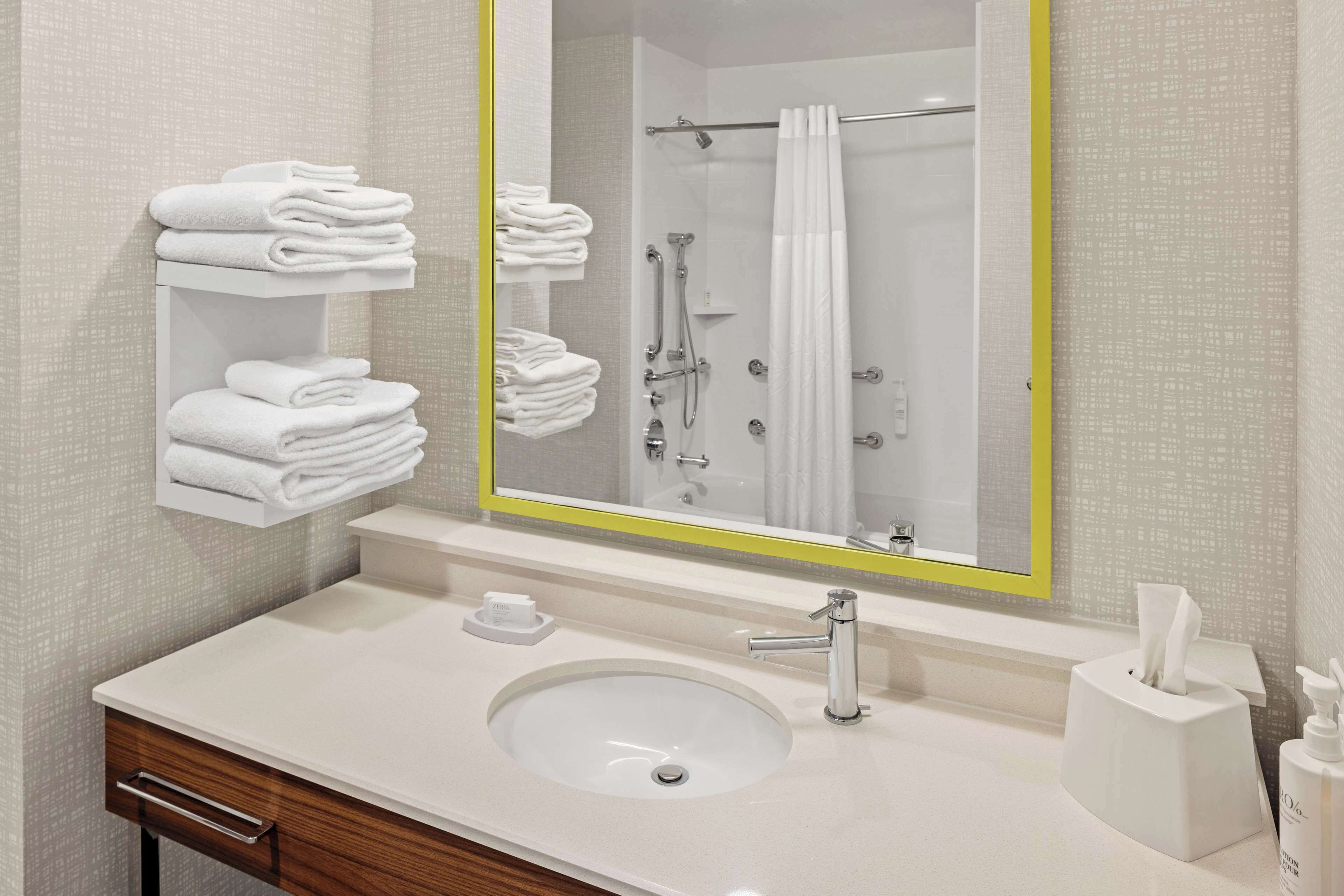 Un baño con un lavamanos blanco, un espejo con marco amarillo y una ducha con cortina blanca.