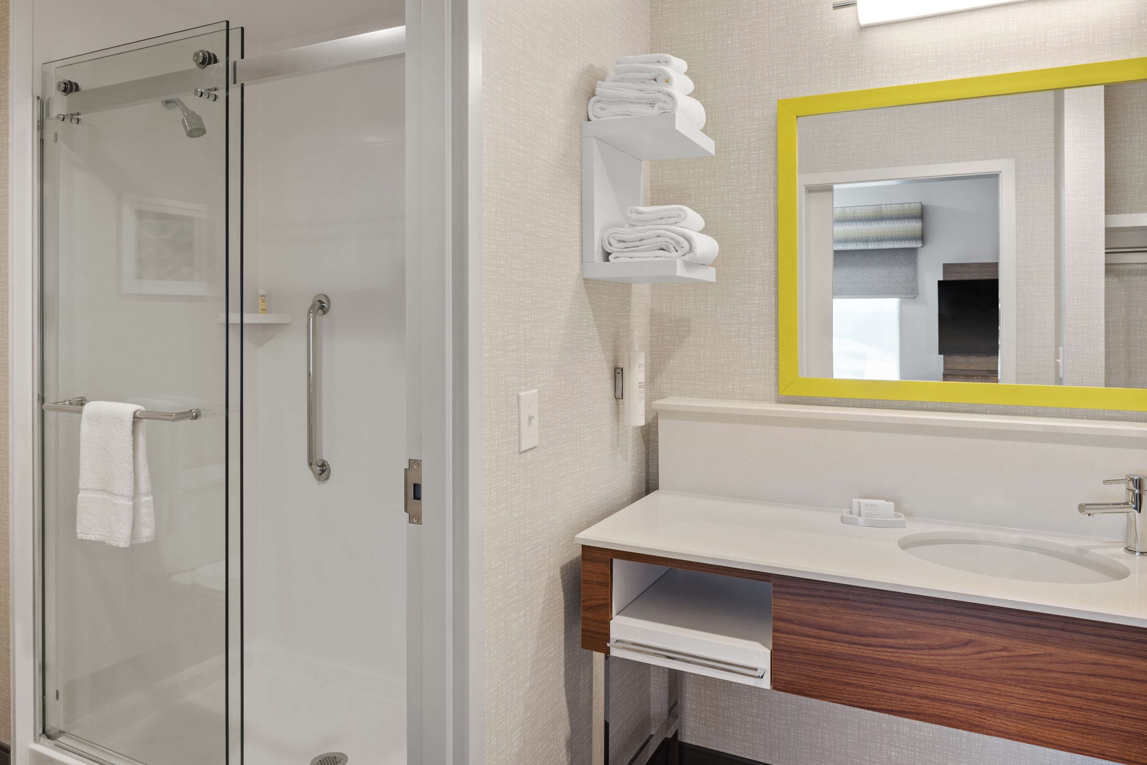 A modern bathroom with a glass-enclosed shower, a white sink with a wooden vanity, and a mirror with a yellow frame.