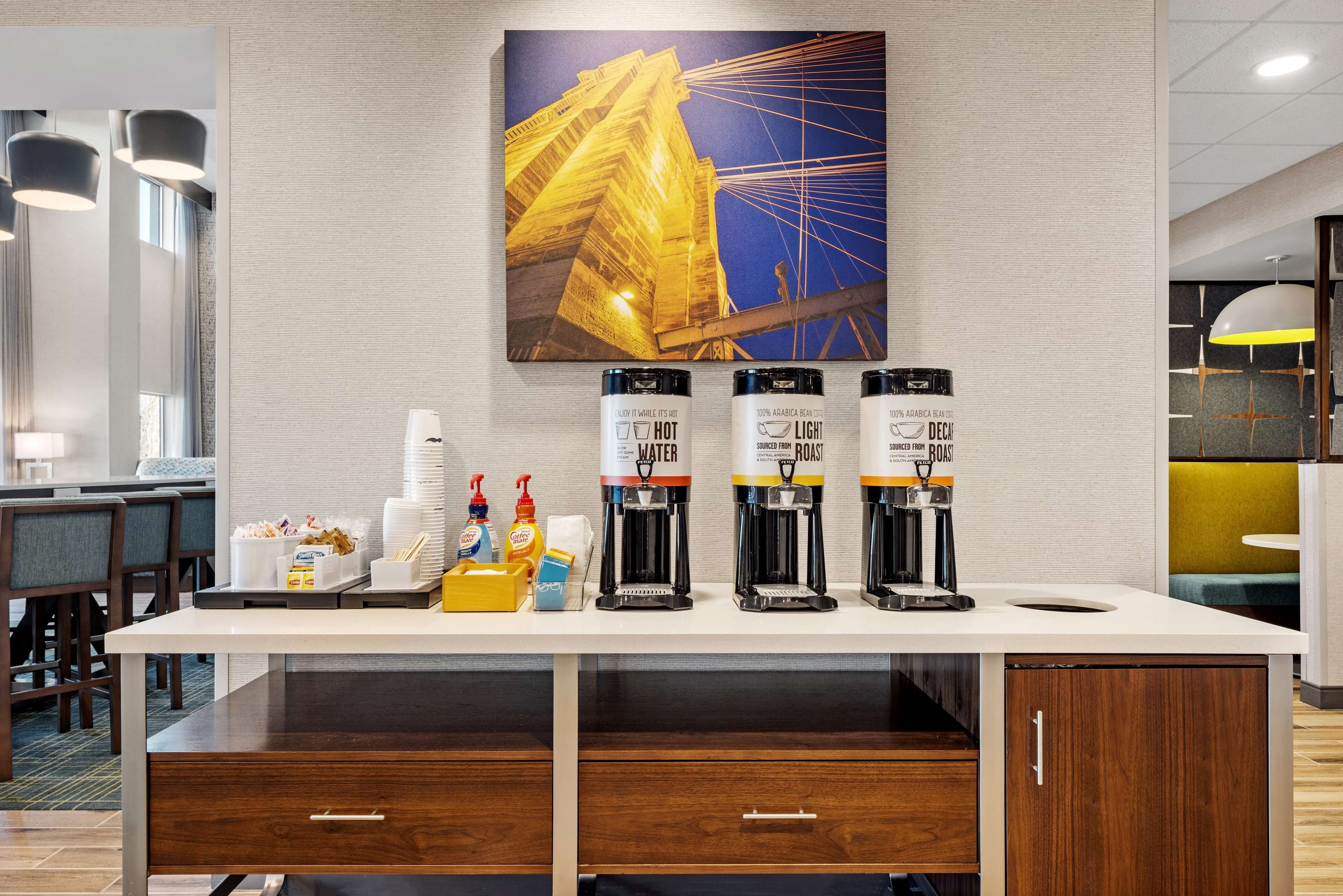 Zona de recepción de hotel con una estación de café, un cuadro de un edificio y un mostrador con servicios.