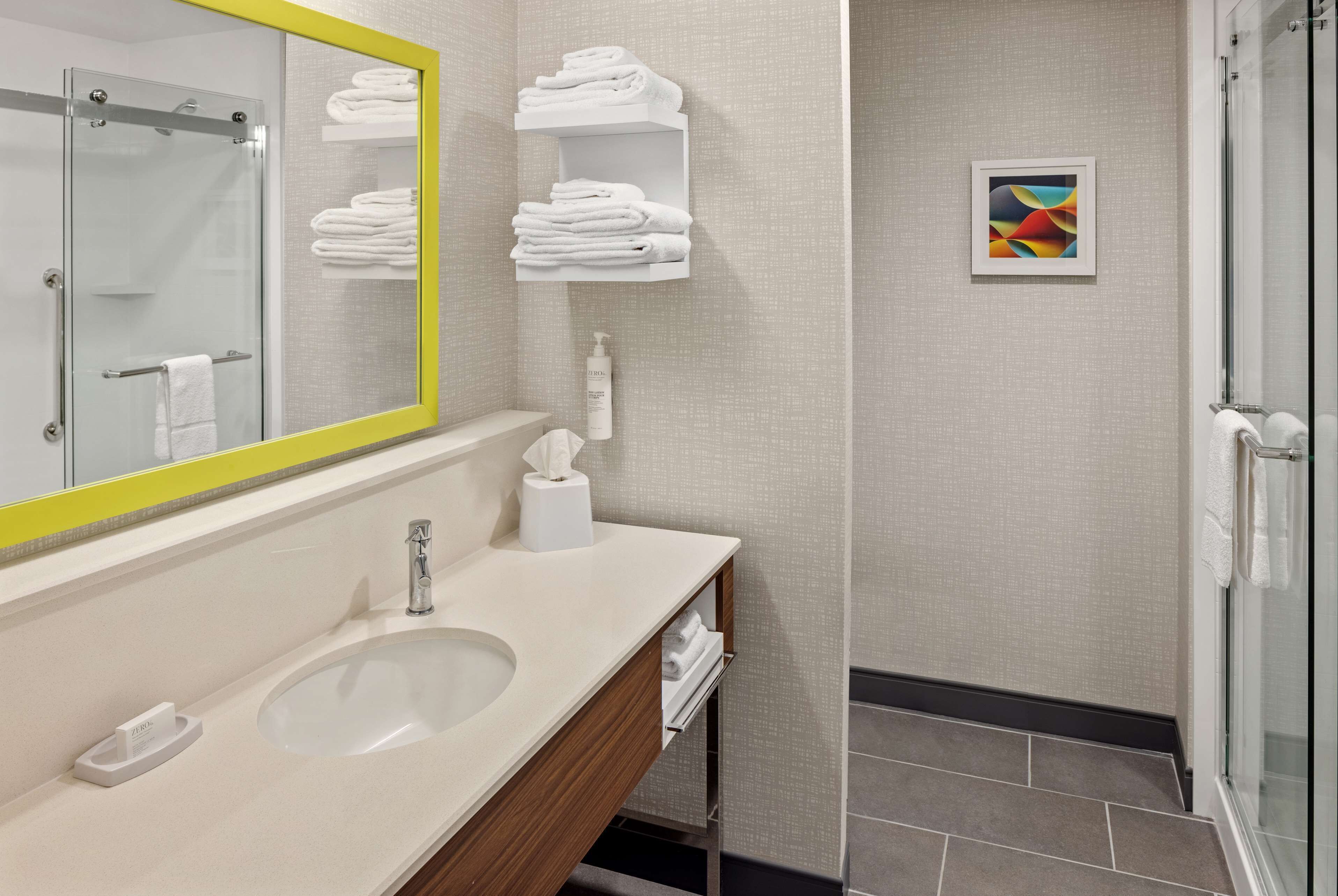 Une salle de bain moderne avec un grand miroir, un lavabo, un porte-serviettes et un espace douche.