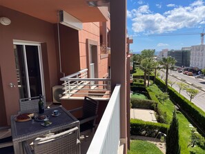 A balcony with a table set for dining, a window, and a view of the street and greenery below. - Ocean Coast – “Apartment” in a private residential complex, 5 minutes from the beach, with private parking (Portimao)