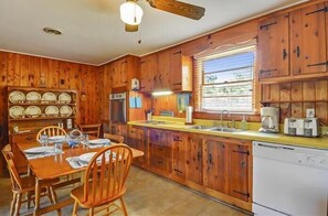 Una cucina in legno con un tavolo da pranzo per quattro persone, un frigorifero e una finestra con persiane.