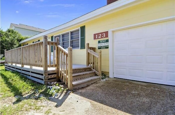 Uma casa térrea com deck de madeira, porta de garagem e uma placa com '123 RENT'.