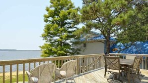 Um deck de madeira com mobiliário ao ar livre, uma piscina e vista para a água.