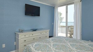 Quarto com cama, cômoda, televisão e varanda com vista para o mar.
