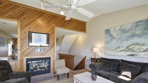 Una sala de estar acogedora con chimenea, un cuadro grande y un ventilador de techo.